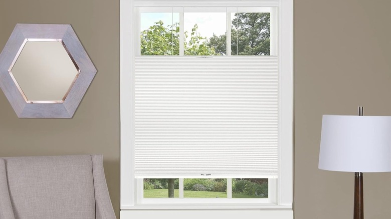 White top-down blinds cover part of a window in a beige minimalist livingroom.