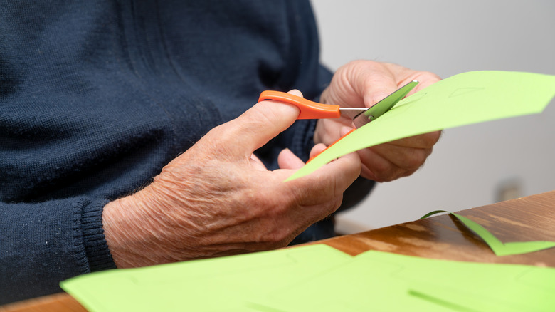 A closeup of a senior's hand cutting paper