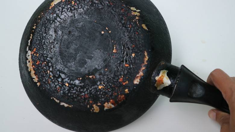 A closeup of a hand holding a burnt skillet