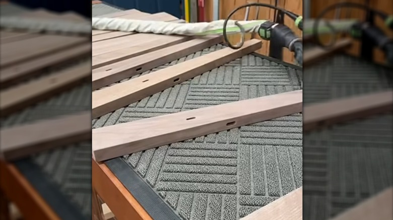 Wood pieces on top of a grey doormat next to a sander