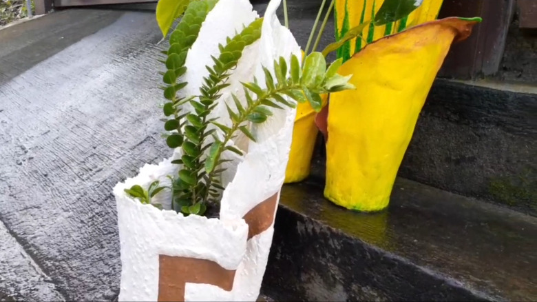 Textured white planter and yellow planter holding ferns on a set of steps