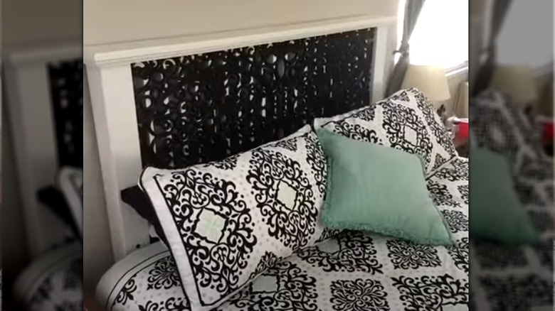 White wooden slat headboard covered with black rubber mat with decorative motif and paired with fleur de lis bedding