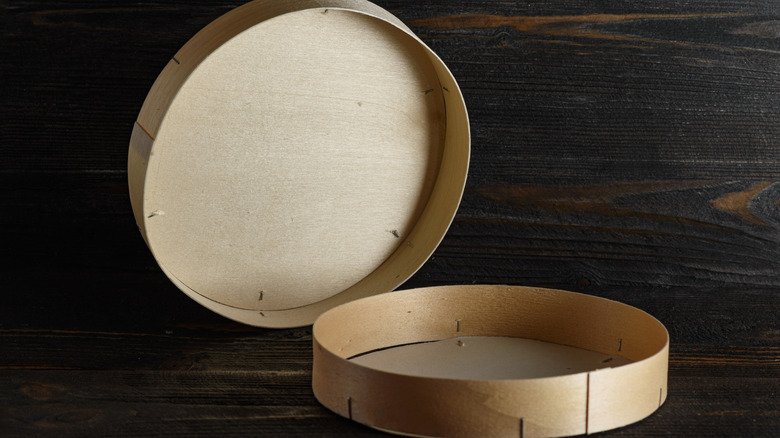 Empty, open circular wood cheese box against dark background