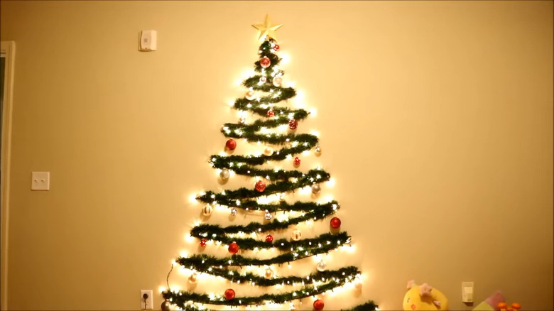 Garland forms a Christmas tree with ornaments on the wall and is bathed in the warm glow of lights