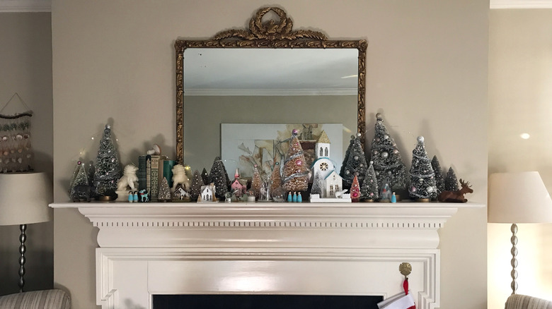 A mantle is decorated with a series of bottle brush trees and miniature houses for Christmas