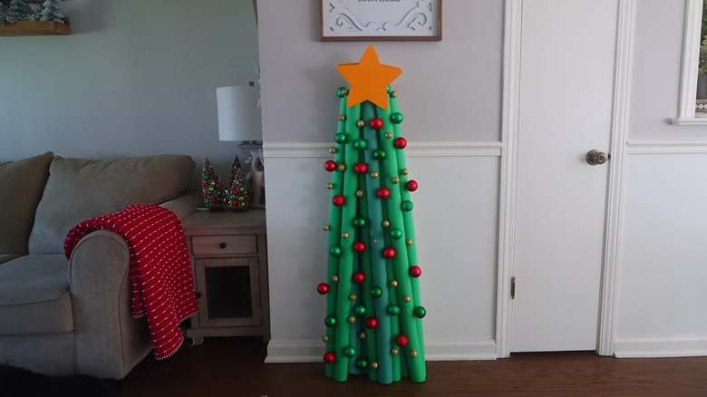 A pool noodle Christmas tree is decorated with a wooden yellow star