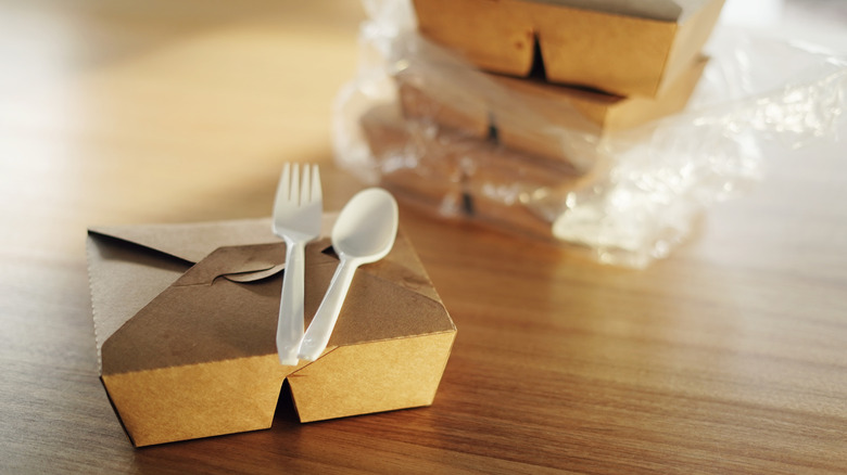 Black plastic cutlery on top of a cardboard takeout box