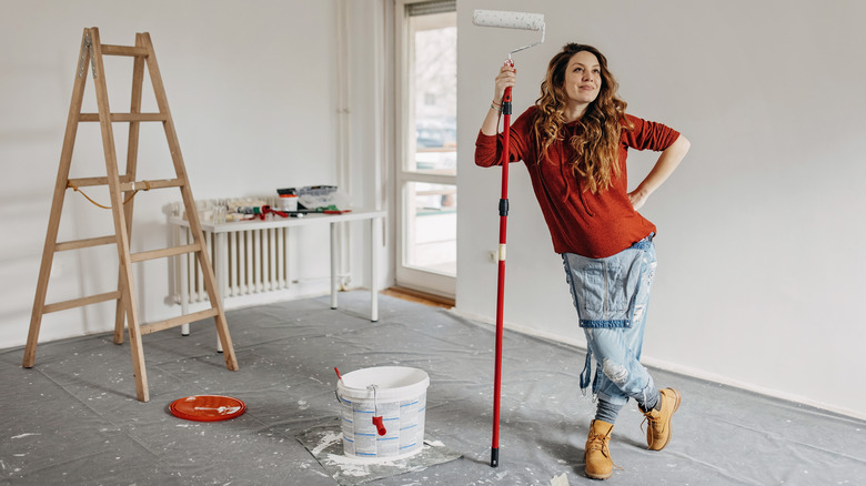 Satisfied woman leaning on a paint roller looking up at her walls