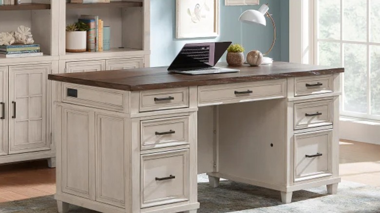 An off-white farmhouse-style desk with dark wood top sits in a home office