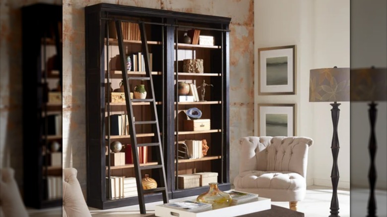 Two tall black bookshelves are placed side-by-side with a library ladder leaning on the metal bar that holds them together.