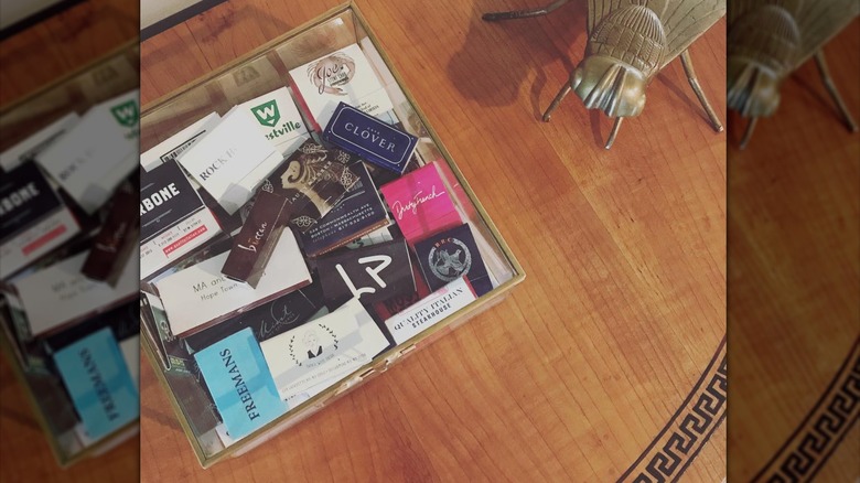 Acrylic box filled with various matchbooks next to a large gold metal bee on a table