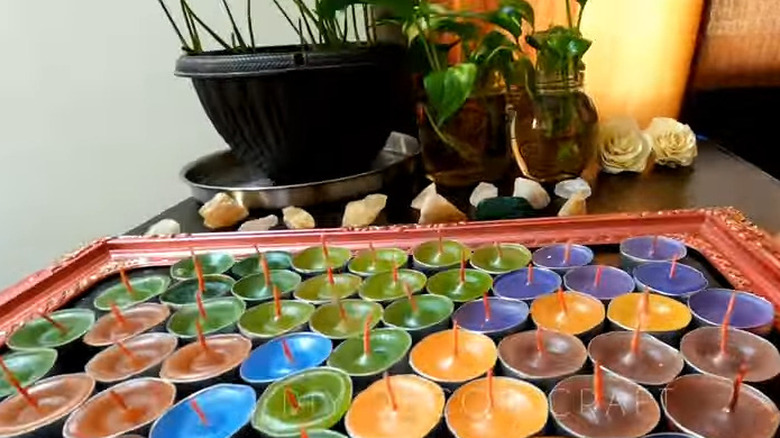 Tea light candle cups each filled with crayon candles sitting on a tray, crystals on the counter behind them