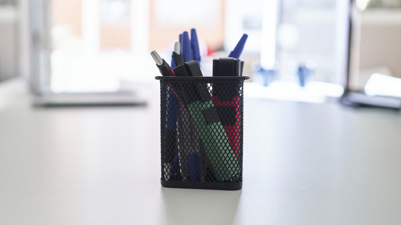 pens, pencils, and markers in a storage cup on a desk