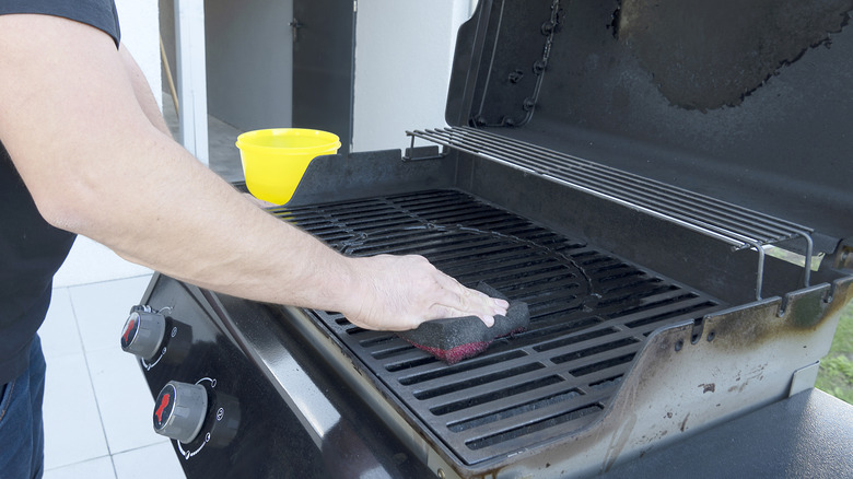 The male hand cleans the black grill with a soft brush.