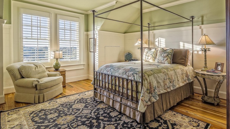 A bedroom with green painted ceilings and walls filled with a four poster bed and big armchair.