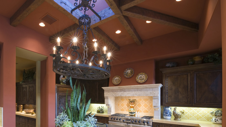 Kitchen with rust red walls and natural wood beams surrounding a skylight.