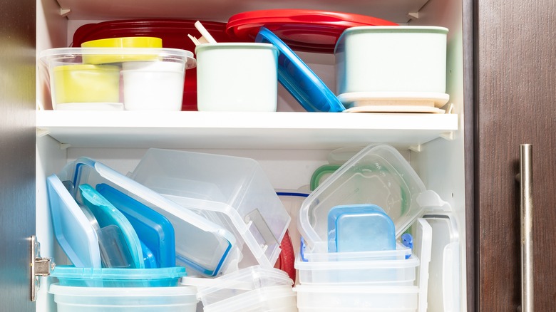 A disorganized cabinets with plastic containers and lids