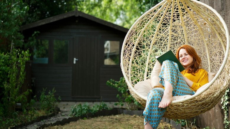 A woman reading a book while relaxing alone in a hanging chair.