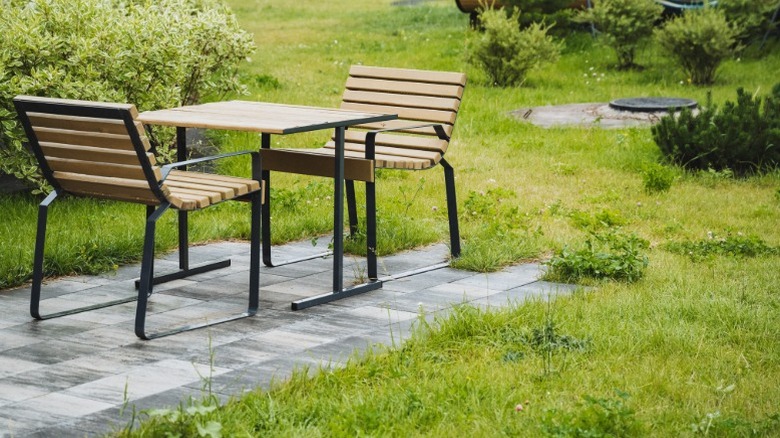 A modern square outdoor table with two modern chairs made with metal and sleek wood.