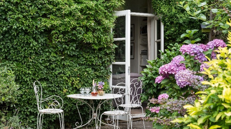 A delicate table and chair set next to an ivy-covered spot in a garden.