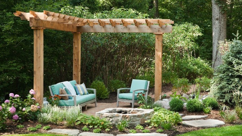 A half pergola with a small sitting area at the edge of a garden.