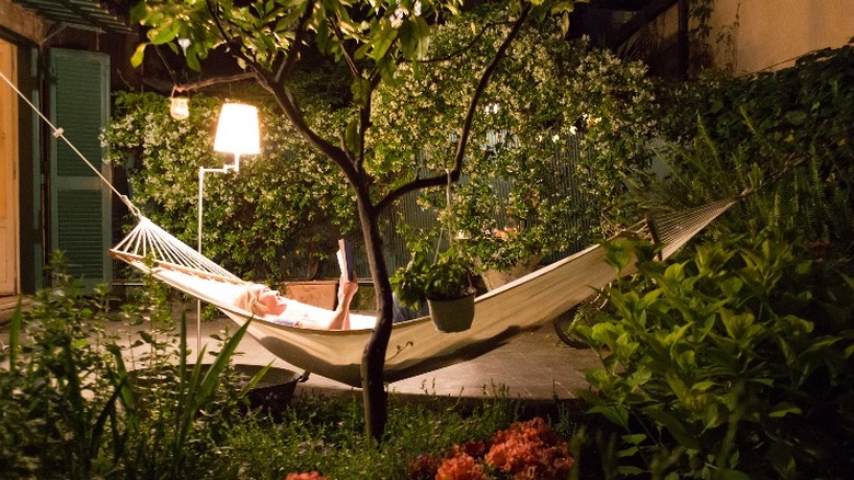 A woman lounging on a traditional canvas hammock in a garden at night.