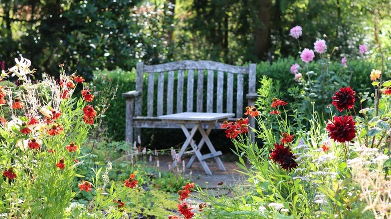 A rustic wooden bench with a small table in them middle of a flower garden.