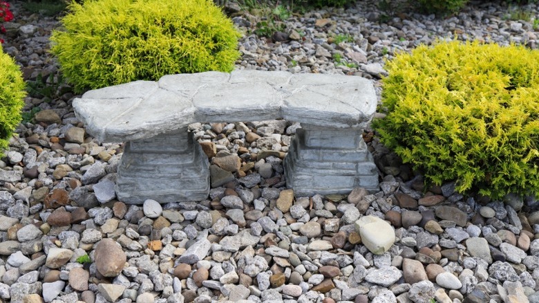 A stone bench sitting amidst shrubs and pebbles.