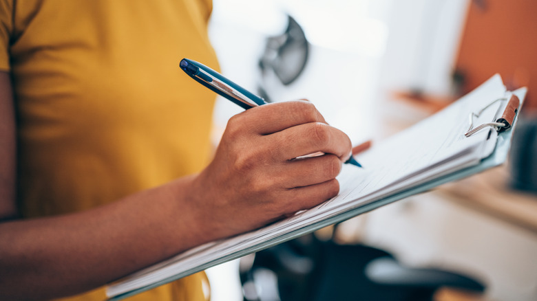 woman writing list on clipboard