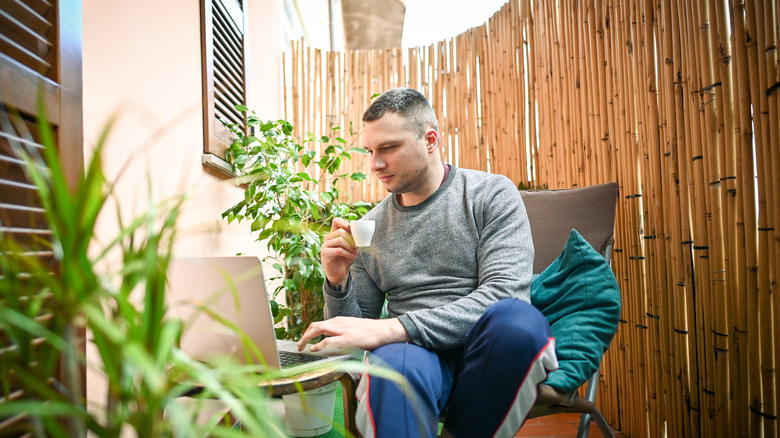 Man sitting in a small backyard near a bamboo privacy fence