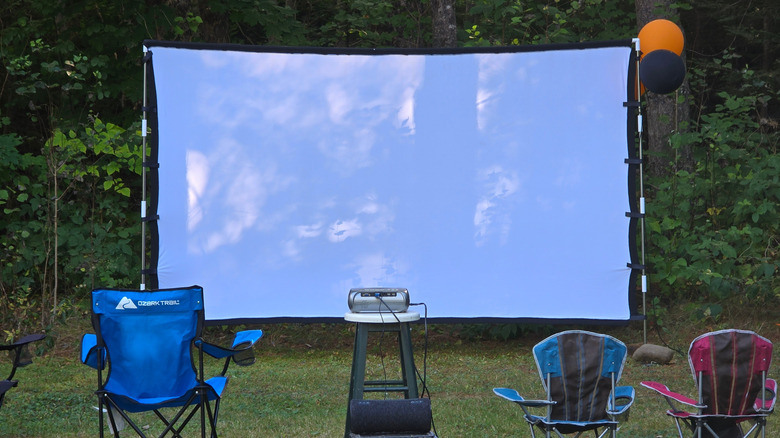 A large white movie screen projector and chairs outside