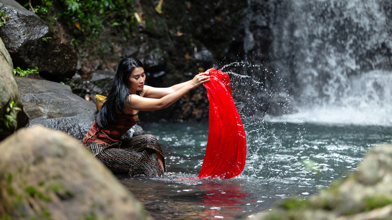 Woman washing dirty clothes near waterfall