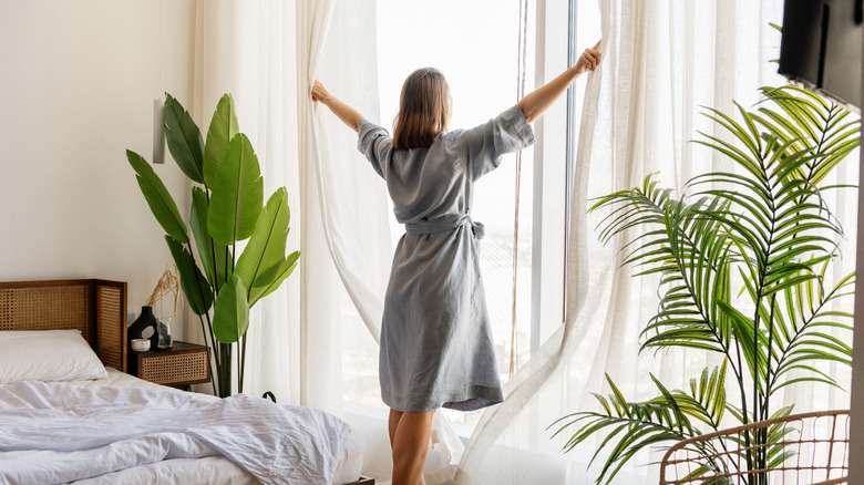 woman pushing open sheer curtains in sunlight