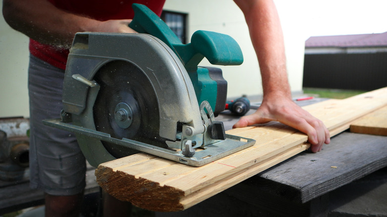 A person using a circular saw to cut wood plank