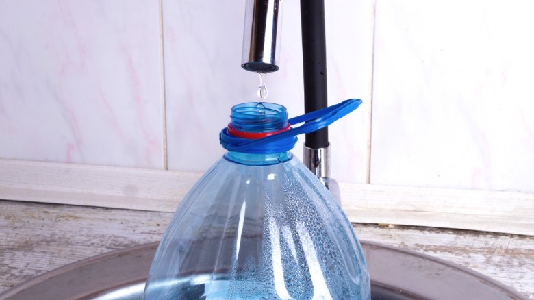 Modern tap dripping into large plastic water bottle in sink