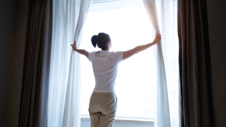 Woman opening curtains on a sunny day