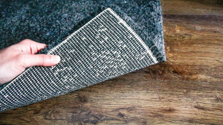 Person holding back corner of plush blue rug on hardwood floor