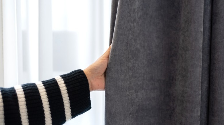 Woman's arm reaching to pull thick gray blackout curtain in front of window