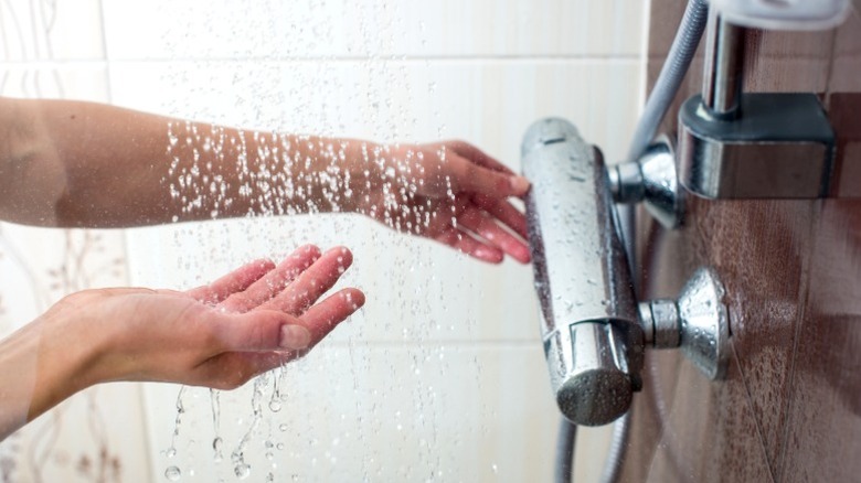 Woman feeling shower water while adjusting temperature with other hand