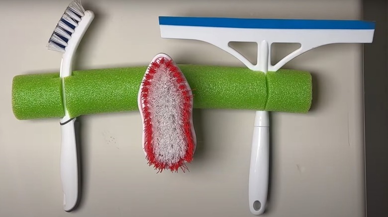 A green pool noodle cleaning supply holder mounted to the wall