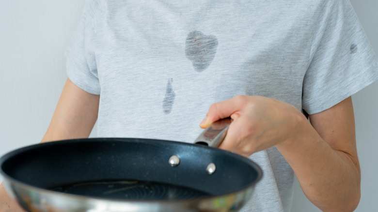 Person with an oil stain on their shirt holding a pan