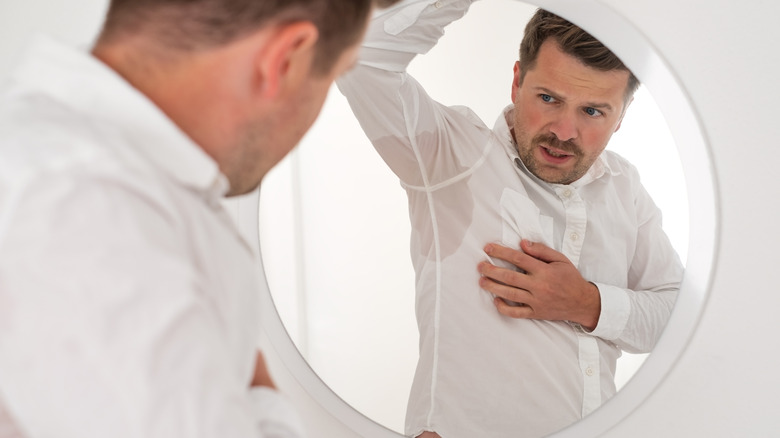 Man wearing a white shirt looking at a sweat stain under his arm