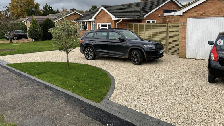 Red brick house with a gravel driveway and brick edging has two cars parked in the driveway.