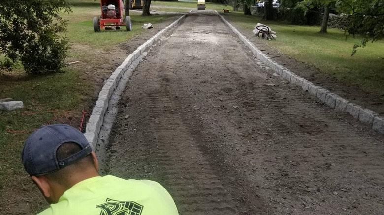 Person laying down cobblestone to edge a driveway.