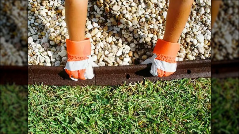 Person installing rubber edging material between gravel and grass wearing gloves