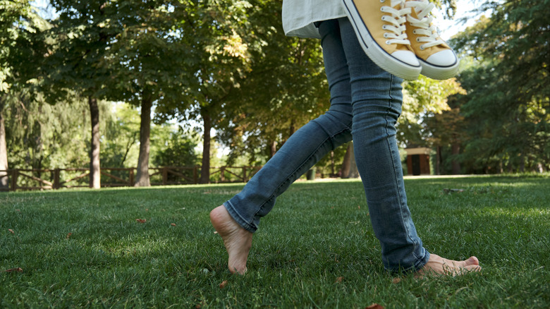 Person walking on barefoot on grass and holding sneakers in their hand