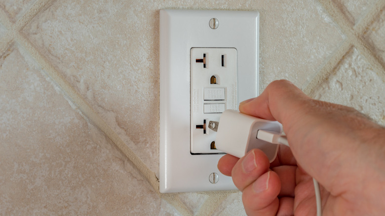 person plugging phone into 20-amp outlet