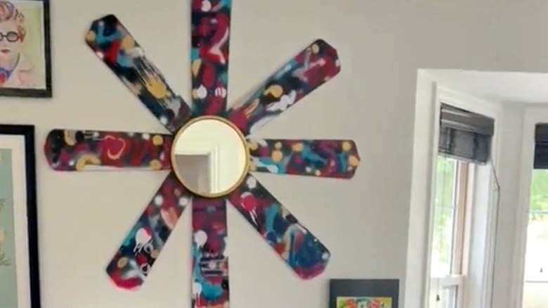 Sunburst mirror made from old ceiling fan blades on a wall surrounded by other artwork