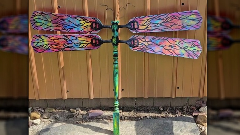 Ceiling fan blades converted to dragonfly art propped against a fence