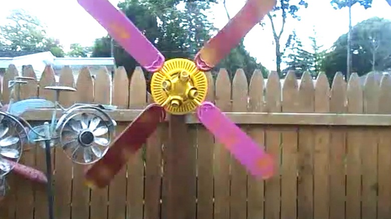 Old ceiling fan converted to a pink and yellow windmill in a backyard